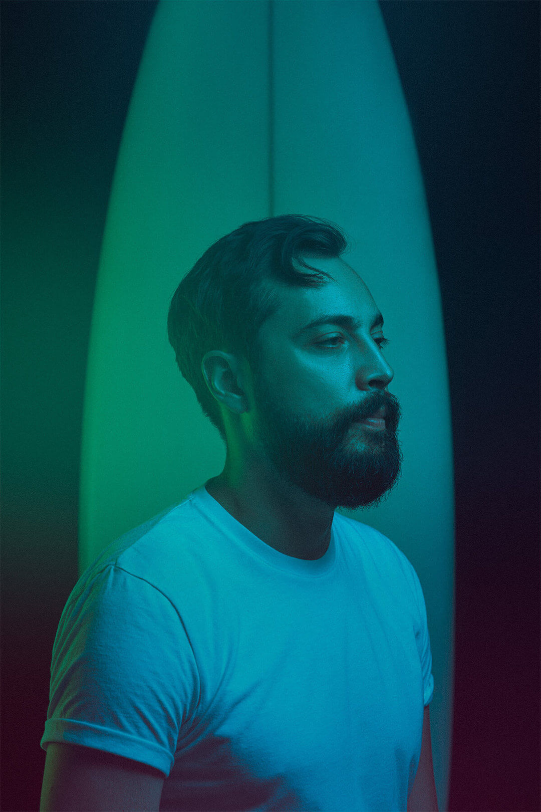 Bearded man with a surfboard in a neon photo session