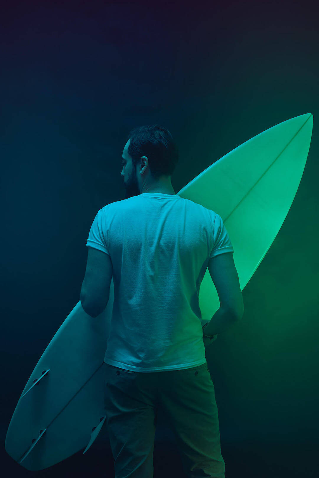 Bearded man with a surfboard in a neon photo session